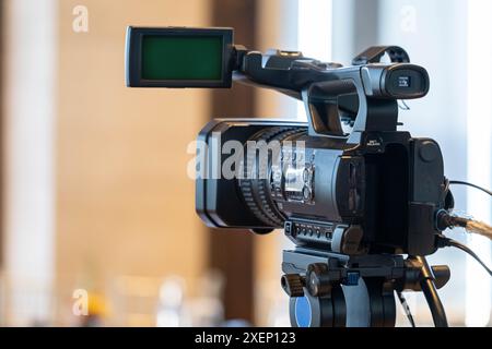 Gros plan d'une caméra vidéo professionnelle sur un trépied avec un écran vert sur l'écran, installé à l'intérieur. Banque D'Images