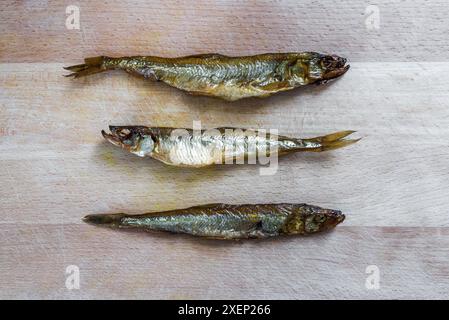 Trois poissons éperlan séchés posés sur Une planche à découper en bois. Vue de dessus Banque D'Images