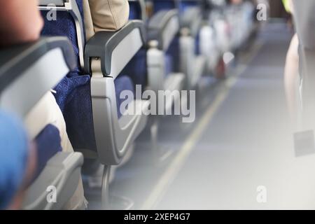 Une rangée de sièges s'étend dans la distance d'un côté de l'avion. Les gens sont assis dos à la caméra dans la cabine passager le long de l'allée. Avec espace à copier. Photo de haute qualité Banque D'Images