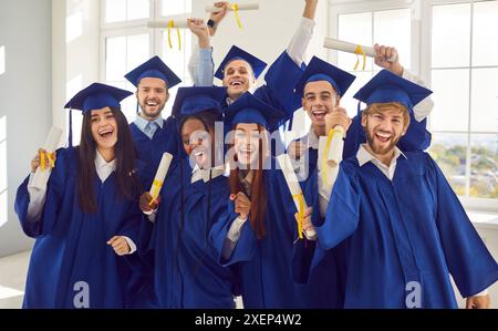 Groupe de rires heureux diplômés multiraciaux debout à l'intérieur détenant un diplôme. Banque D'Images