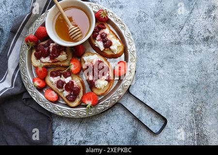 Sandwich avec fraises, fromage à pâte molle et miel sur planche de bois sur fond gris. Vue de dessus . Banque D'Images