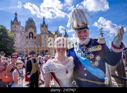 Schwerin, Allemagne. 29 juin 2024. Le grand-duc Friedrich Franz II et la grande-duchesse Marie von Mecklenburg-Schwerin arrivent avec de nombreux invités costumés dans le style de la mode crinoline (vers 1840 - 1869) après le défilé historique devant le château. Le festival du château est célébré dans la capitale de l'État de Mecklembourg-Poméranie occidentale le week-end. En plus d'une représentation de l'association du château, les visiteurs seront attirés par un marché d'art et d'artisanat, un spectacle de lumière et de musique en soirée et une journée portes ouvertes au parlement de l'État. Crédit : Jens Büttner/dpa/Alamy Live News Banque D'Images