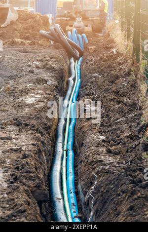 Nouveau conduit de service posé dans la tranchée ouverte pour remplacer la nouvelle conduite d'eau et fournir de nouveaux câbles électriques pour les points de recharge des véhicules électriques Banque D'Images