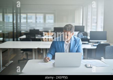 Homme d'affaires d'âge moyen occupé travaillant sur ordinateur portable dans le bureau écrivant des notes. Banque D'Images