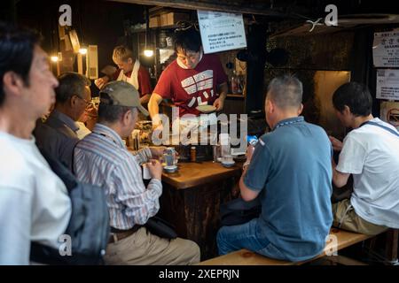 Tokyo, Japon - 15 juin 2024 : les clients se régalent de la cuisine japonaise à Omoide Yokocho, une ruelle populaire avec des stands de nourriture situés dans la ville de Shinjuku Banque D'Images