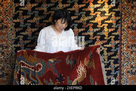 (240629) -- PÉKIN, 29 juin 2024 (Xinhua) -- Ji Yu montre un tapis de palais dans son atelier à Pékin, capitale de la Chine, le 27 juin 2024. Le tapis du palais de Pékin est un magnifique exemple des techniques traditionnelles de tissage de tapis de Chine. Connu pour ses processus de production complexes et ses beaux motifs, le tapis du palais représente le summum de l'art du tissage chinois. La production comprend quatre étapes principales : teinture avec des herbes traditionnelles chinoises, création de patrons, tissage et façonnage, et enfin, finitions. Comme l'un des 'huit artisanats impériaux de Pékin', l'art du tapis de palais était de Banque D'Images