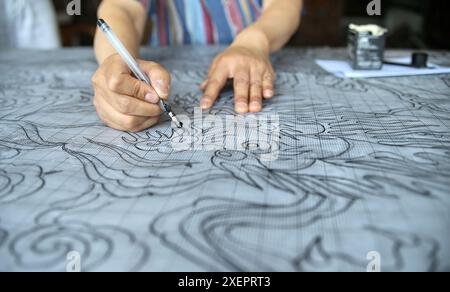 (240629) -- PÉKIN, 29 juin 2024 (Xinhua) -- Ji Yu dessine un motif pour un tapis de palais dans son studio à Pékin, capitale de la Chine, le 27 juin 2024. Le tapis du palais de Pékin est un magnifique exemple des techniques traditionnelles de tissage de tapis de Chine. Connu pour ses processus de production complexes et ses beaux motifs, le tapis du palais représente le summum de l'art du tissage chinois. La production comprend quatre étapes principales : teinture avec des herbes traditionnelles chinoises, création de patrons, tissage et façonnage, et enfin, finitions. Comme l'un des huit artisanats impériaux de Pékin, l'art de Banque D'Images