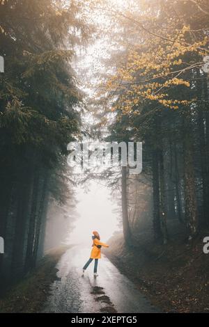 Dans la paisible forêt d'automne, une femme seule marche le long d'un sentier couvert de brume, profitant de la beauté sereine de la nature pendant son aventure en plein air. Banque D'Images