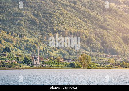 À Plav, au Monténégro, une mosquée surplombe le lac tranquille, se fondant dans le paysage pittoresque des Balkans et son architecture traditionnelle. Banque D'Images