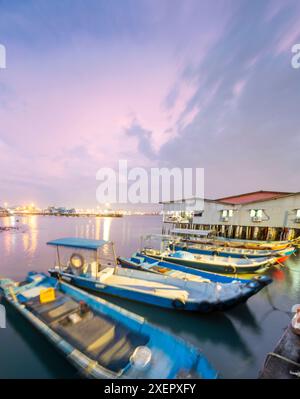 Beau ciel rose, petits bateaux qui bougent dans les eaux calmes du détroit de Malacca, et vieux bâtiments de jetée en bois, éclairés le long de la promenade à dus Banque D'Images