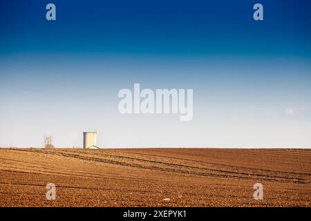 Image d'un champ labouré avec des sillons sur un après-midi ensoleillé avec un ciel bleu en serbie, dans deliblatska pescara avec un silo en arrière-plan. Cette image feat Banque D'Images