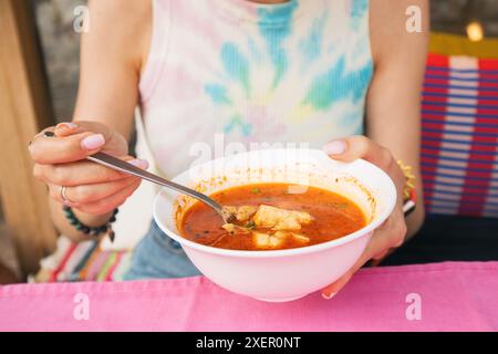 Une femme mange de la soupe dans un bol blanc. Elle tient une cuillère à la main Banque D'Images