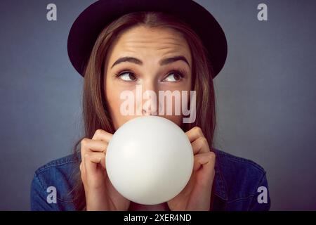 Fête, ballon et femme avec soufflage en studio pour le plaisir, le plaisir et la célébration sur fond bleu. Organisateur d'événements, réflexion et personne avec Banque D'Images