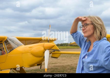 Une femme blonde dans des lunettes sur la piste sur le fond d'un avion jaune vintage et un ciel orageux Banque D'Images