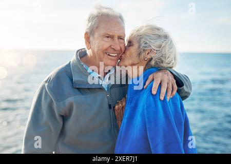 Couple aîné, les gens et la joue embrassent dans l'océan avec soutien, amour et affection pour la pause au Canada. Relation, date et heureux ou sourire pour Banque D'Images