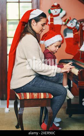 Mère, piano et enfant à la maison pour les vacances de Noël, l'enseignement et le lien avec le soutien, l'amour ou les soins. Femme, fils et jouer au clavier ensemble dans la maison Banque D'Images