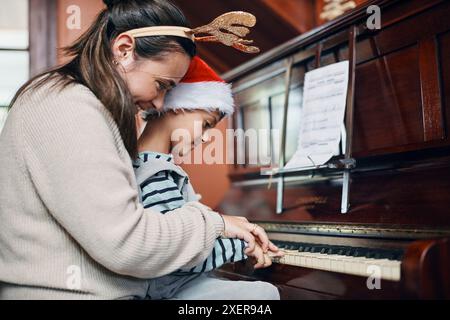 Mère, garçon et piano à Noël à la maison avec le sourire, l'amour ou l'apprentissage pour la musique, la performance ou les notes. Maman, enfant ou fils par clavier pour l'enseignement Banque D'Images