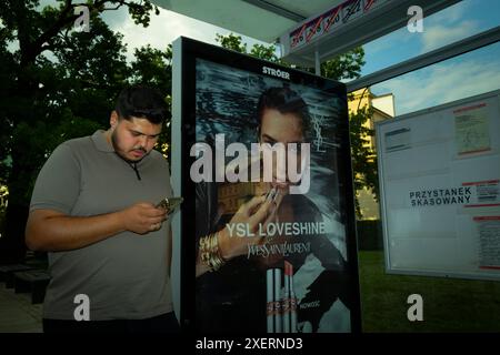 Varsovie, Pologne. 28 juin 2024. Un homme est vu regarder son téléphone portable à côté d'une publicité pour les cosmétiques Yves Saint Laurent à Varsovie, en Pologne, le 28 juin 2024. (Photo de Jaap Arriens/Sipa USA) crédit : Sipa USA/Alamy Live News Banque D'Images