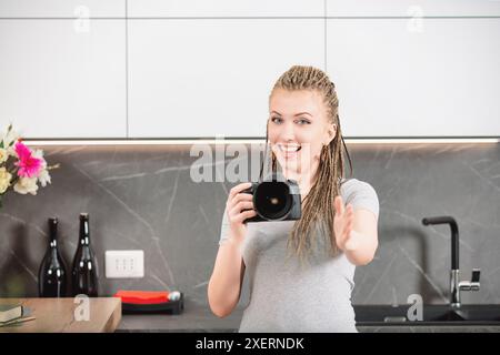 Photographe féminin avec des cheveux tressés instruit quelqu'un sur la pose tout en tenant un appareil photo. Son sourire et son geste indiquent une orientation claire, assurant le Banque D'Images