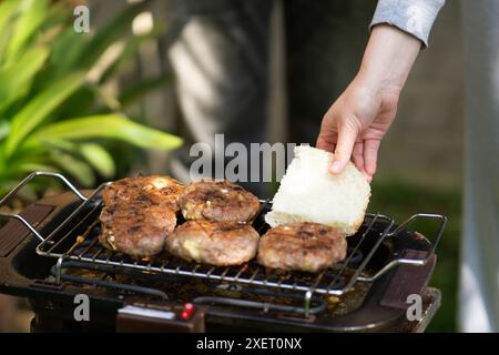 femme mettant du pain blanc sur le barbecue avec des hamburgers Banque D'Images