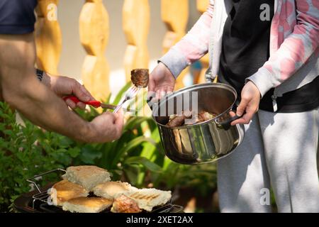 Homme et femme ramassant la viande grillée du barbecue dans un pot en métal. Banque D'Images