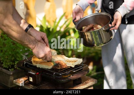 Homme et femme ramassant la viande grillée du barbecue dans un pot en métal. Banque D'Images