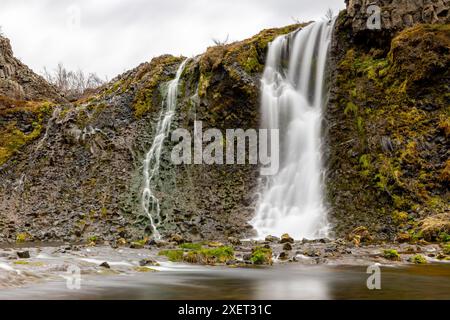 Cascade et étang entourés de colonnes de basalte et de formations rocheuses volcaniques, pierres envahies de mousse dans le canyon de Gjain dans la vallée de Þjórsárdalur, Icela Banque D'Images