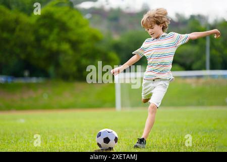 Enfant jouant au football. Les enfants jouent au football sur un terrain extérieur. Petit garçon donnant un coup de pied au ballon dans le parc d'été. Activité saine pour les jeunes enfants. Sport scolaire Banque D'Images