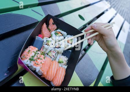 Une femme tient une paire de baguettes ramassant un rouleau de sushi dans une assiette de sushi de fruits de mer fraîchement préparés sur un stand de Street food London Covent Garden UK Banque D'Images