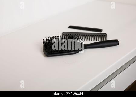 Brosse à cheveux et peignes utilisés avec quelques cheveux sur la table blanche, hygiène de la peau de la tête Banque D'Images