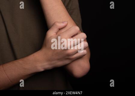 Jeune homme se grattant le bras avec sa main. Maladie de la peau. Irritation, allergie. Isolé sur fond noir. Banque D'Images