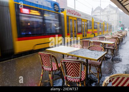 Un train passe devant un restaurant avec des tables et des chaises à l'extérieur. Les chaises sont rouges et jaunes, et les tables sont recouvertes de tissus rouges et blancs Banque D'Images