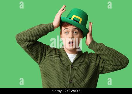 Jeune homme choqué dans le chapeau de leprechaun sur fond vert. Célébration de la fête de Patrick Banque D'Images