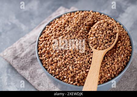 Grains de sarrasin en cuillère en bois sur fond gris, gros plan Banque D'Images