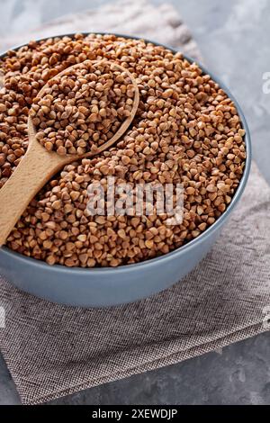 Grains de sarrasin en cuillère en bois sur fond gris, gros plan Banque D'Images