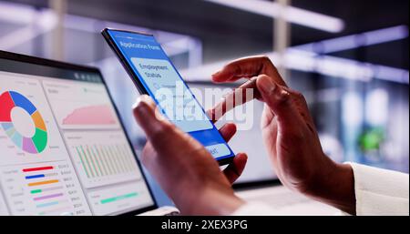 African American Student remplit la demande de bourse en ligne en utilisant un téléphone noir et un ordinateur portable intelligent au bureau du Collège Banque D'Images