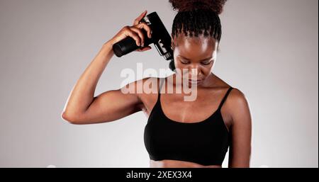 Physiothérapeute sportif utilisant la machine à pistolet de massage pour la thérapie de récupération sur la mauvaise posture de la femme afro-américaine après l'entraînement Banque D'Images