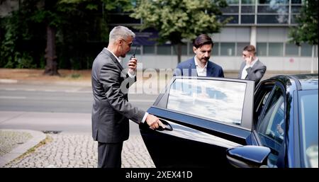 Les gardes du corps d'entreprise assurent une sortie sûre pour l'homme d'affaires dans un véhicule de luxe avec chauffeur, services de protection VIP, équipe de sécurité en costumes. Banque D'Images