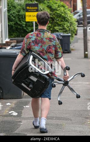 Selly Oak, Birmingham, 30 juin 2024 - Un étudiant prend une chaise de jeu cassée au bout d'une route. - Les rues résidentielles de Birmingham ont été transformées en décharges car les étudiants déménagent à la fin de leurs contrats. La plupart des étudiants fréquentent l'Université de Birmingham qui est à environ 800 mètres des rues résidentielles en terrasses Selly Oak. Les routes ont principalement été achetées par les propriétaires qui les louent aux étudiants de premier cycle avec rangée sur rangée de panneaux «pour louer». Crédit : arrêtez Press Media/Alamy Live News Banque D'Images