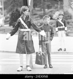 Patrouille de sécurité junior dans les années 1960 Une adolescente se tient debout, les bras sortis, et signale aux piétons de s'arrêter au passage. Lorsque les voitures sont passées ou arrêtées, les enfants peuvent traverser la rue à pied. Faire partie de la patrouille de sécurité junior était volontaire pour les élèves de l'école et la récompense était parfois de faire des voyages et des excursions plus courts. De nos jours, l'opération est fermée dans de nombreuses municipalités. Suède 1964 Banque D'Images