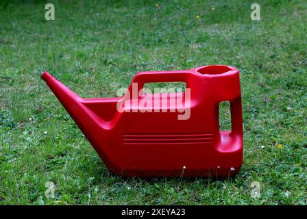 Vieil arrosoir en plastique rouge sur une pelouse de jardin de banlieue unkempt Banque D'Images