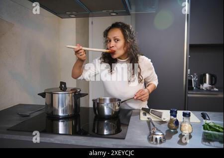 Belle femme appréciant la nourriture parfaite, signe de main bellissimo, tester la sauce pour pâtes tomate pour le goût, cuisiner le dîner dans la couleur grise hom minimaliste Banque D'Images