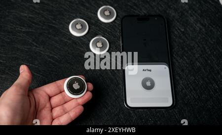 Jurmala, Lettonie - 25 06 2024 : la femme tient AirTag dans ses mains, et les clés de l'appartement sont floues dans le fond noir. Aide sur les étiquettes aériennes Banque D'Images