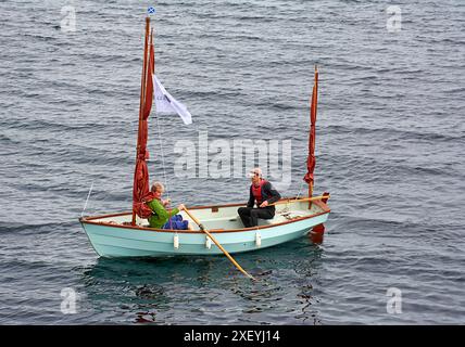 Portsoy Boat Festival un petit bateau à rames aux voiles brunes et deux marins quittant le port Banque D'Images