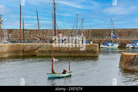 Portsoy Boat Festival petit bateau à rames avec des voiles brunes et deux marins quittant le port Banque D'Images