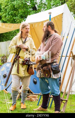 Deux reconstituteurs historiques habillés en guerriers anglo-saxons debout parlant devant quelques lances sur un rack et une tente. Sandwich Centre médiéval. Banque D'Images