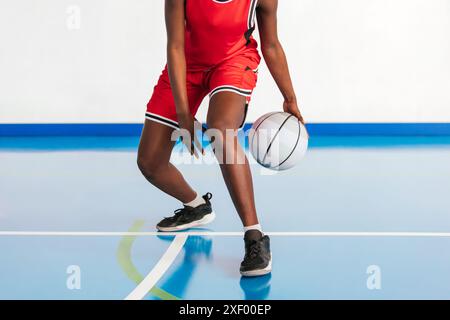 Gros plan photo horizontal d'une joueuse de basket-ball dans un uniforme rouge pratiquant des techniques de dribble sur un court couvert, mettant en valeur l'agilité, la concentration, et Banque D'Images