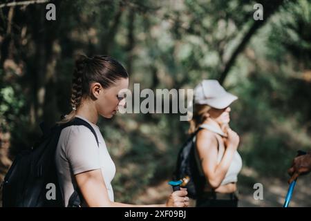 Deux femmes marchant à travers un sentier forestier, équipées de sacs à dos et de bâtons de trekking Banque D'Images