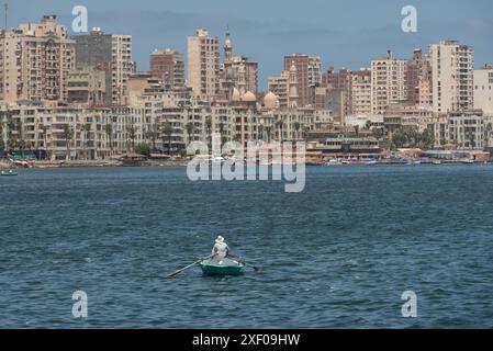 Alexandrie, Égypte. 26 juin 2024. Un seul pêcheur égyptien dans un petit bateau pêchant dans la mer Méditerranée avec la ligne d'horizon d'Alexandrie en arrière-plan, la deuxième plus grande ville d'Égypte. (Crédit image : © John Wreford/SOPA images via ZUMA Press Wire) USAGE ÉDITORIAL SEULEMENT! Non destiné à UN USAGE commercial ! Banque D'Images