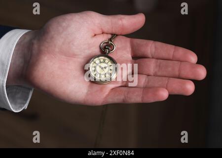 Homme tenant la chaîne avec montre de poche élégante sur fond flou, gros plan Banque D'Images